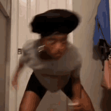 a woman in a gray shirt and black shorts is standing in front of a door and making a funny face .