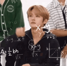 a man is sitting in front of a chalkboard with a bunch of math equations on it .