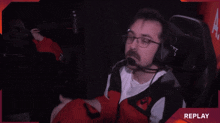 a man wearing headphones and a red jacket is sitting in a chair with the word replay in the upper right corner