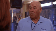 a bald man wearing a blue shirt that says ravens basketball is talking to a woman .