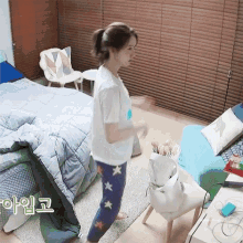 a woman in a white shirt and blue pants is standing in a bedroom near a bed .