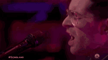 a close up of a man singing into a microphone with #songland on the bottom