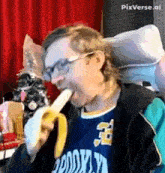 a man wearing glasses is eating a banana while wearing a brooklyn jersey .