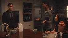 a man and a woman are sitting at a table talking to each other in a kitchen