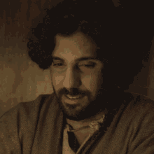 a man with curly hair and a beard is wearing a brown jacket