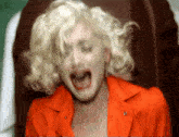 a woman with blonde hair is wearing an orange jacket and screaming