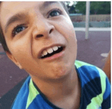 a young boy is smiling and looking up at the camera while wearing a blue and green shirt .