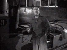 a black and white photo of a man standing in front of a boat with the number 9 on it