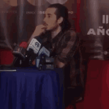 a man sits at a table with microphones in front of a sign that says " año " on it