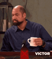 a man with a beard is holding a cup of coffee in front of a victor sign