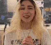 a woman with blonde hair is wearing a white t-shirt with a graphic on it .