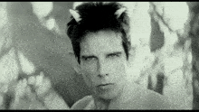 a black and white photo of a shirtless man with horns in his hair
