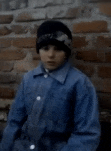 a young boy wearing a black hat and a blue jacket is eating a piece of food .