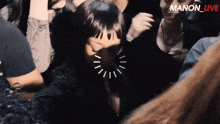 a group of people are gathered in a dark room with the words manon_live on the bottom right