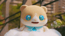 a stuffed animal with blue eyes and a necklace is sitting on a cloud .