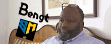 a man wearing glasses sits on a couch with a bengt sm logo in the background