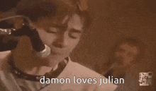 a man is singing into a microphone with the words `` damon loves julian '' written below him .