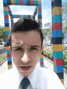 a man wearing a white shirt and tie is standing in front of a colorful sculpture