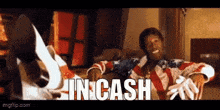 a man in an american flag shirt is sitting on a couch with the words in cash written on the screen