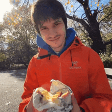 a man wearing a red arcteryx jacket holds a sandwich