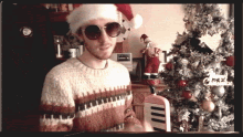 a man wearing a santa hat and sunglasses is standing in front of a christmas tree