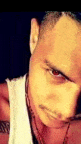 a close up of a man 's face with red eyes and a white shirt