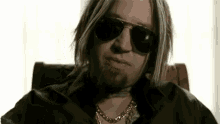 a man with blonde hair and a beard wearing sunglasses and a gold chain .