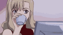 a girl is drinking from a cup while looking at a computer monitor