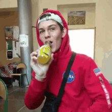 a man in a red nasa hoodie drinks from a can