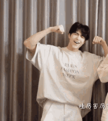 a man wearing a white paris fashion week t-shirt flexes his muscles