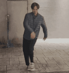 a man wearing a blue jacket and black pants is walking on a sidewalk