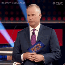 a man in a suit and tie holds a family feud canada sign