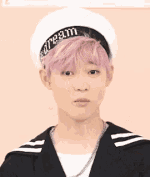 a young man with pink hair is wearing a sailor hat and making a face .