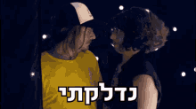 a man in a yellow shirt is standing next to a woman in a black hat with a foreign language written on it