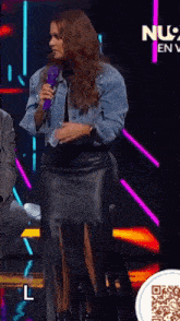 a woman in a leather skirt stands on a stage with a microphone in her hand and the letter l below her