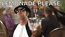 a man in a hat and sunglasses is holding a glass of lemonade while sitting at a table .