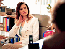 a woman in a white jacket is sitting in a chair with a telephone in front of her