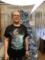 a man wearing a black t-shirt with a fisherman on it stands in front of a decorated christmas tree