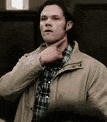 a man in a plaid shirt and jacket is holding his hand to his chin .