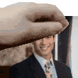 a man in a suit and tie is smiling while a hand holds his head .