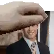 a man in a suit and tie is smiling while a hand holds his head .