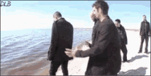a group of men are standing on a beach near the water and talking .