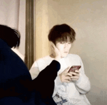 a man is holding a cell phone in his hand while another man looks on .
