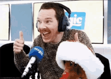 a man wearing headphones is giving a thumbs up next to a stuffed reindeer wearing a santa hat .