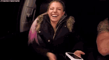 a woman in a black jacket is laughing in the back of a car .