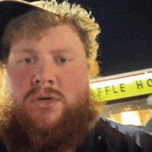 a man with a beard wearing a hat is standing in front of a waffle house .