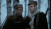 two men in military uniforms are standing in a forest .