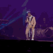 a man in a tan suit is singing into a microphone on a stage .