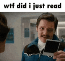 a man with a mustache is holding a picture in his hand and talking to another man .