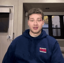 a man in a blue hoodie with a black eye is sitting in a room with a window .